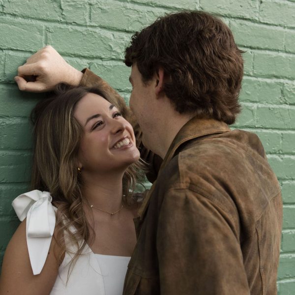 Woman Smiling while looking at her fiance in front of a green wall in City Market in Downtown Raleigh NC - Engagement Session